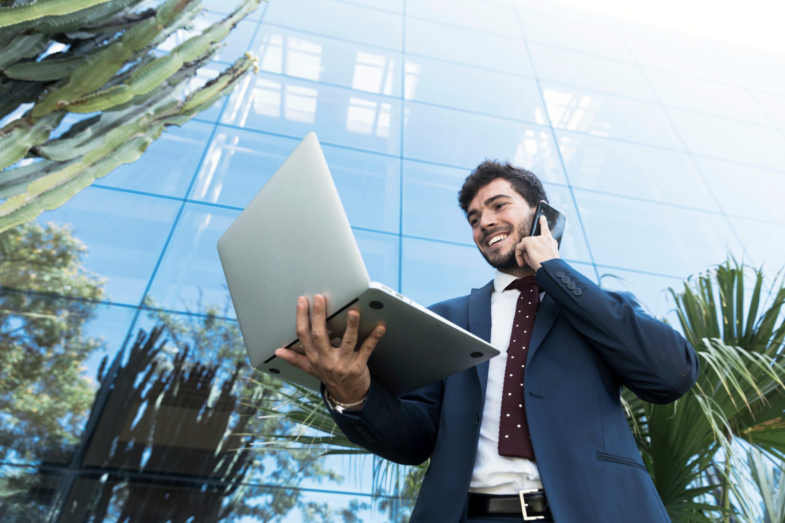 Business owner using laptop and phone outside office building, representing productivity with virtual assistant services in USA